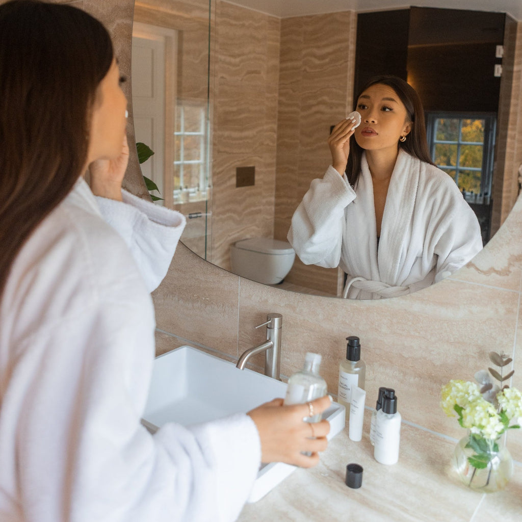 Woman applying Bigelius facial toner to her face in a bathroom. Bigelius skincare facial toner - a balancing, naturally scented cleansing, and hydrating toner. Firms and tones skin with natural herbal extracts and potent antioxidant.