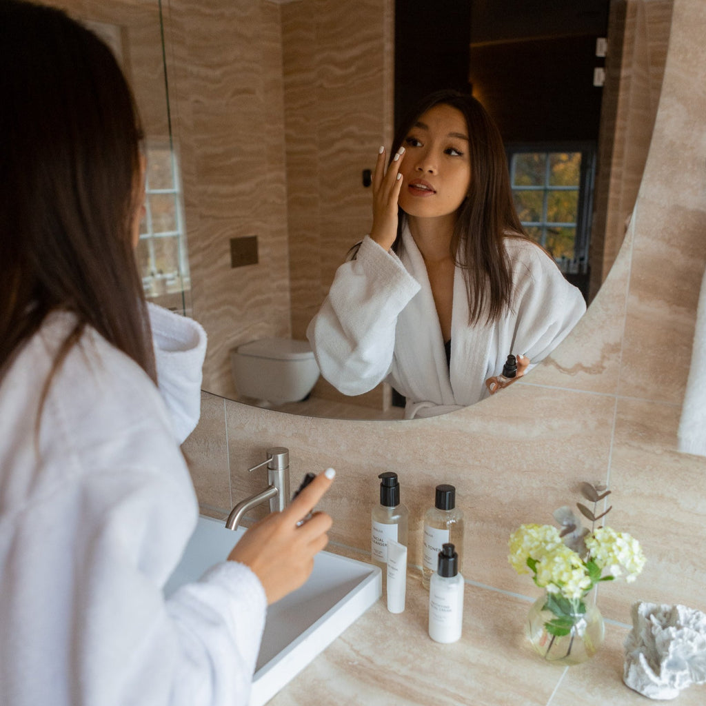 Woman applying Bigelius skincare to her face in a bathroom. A balancing, naturally scented cleansing, and hydrating. Firms and tones skin with natural herbal extracts and potent antioxidant.