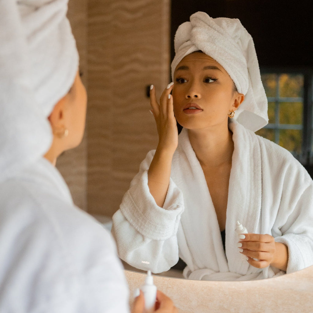 Woman applying Bigelius skincare to her face in a bathroom. A balancing, naturally scented cleansing, and hydrating. Firms and tones skin with natural herbal extracts and potent antioxidant.