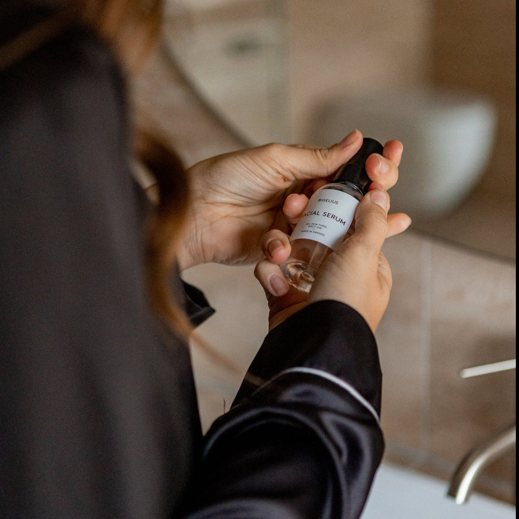 Woman applying Bigelius skincare to her face in a bathroom. A balancing, naturally scented cleansing, and hydrating. Firms and tones skin with natural herbal extracts and potent antioxidant.